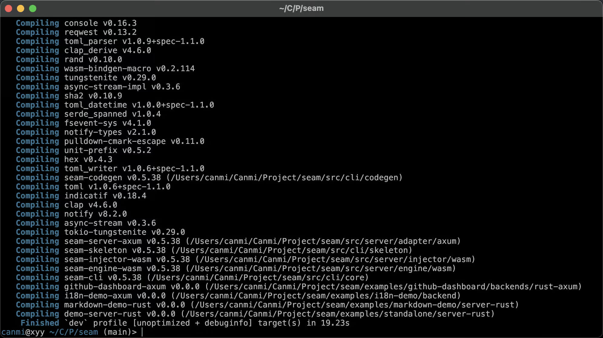 Ein Terminal‑Screenshot zeigt das Ende eines Cargo‑Build‑Logs für einen Rust‑Workspace namens „seam“, der mit `~/C/P/seam` bezeichnet ist und in dem die Shell unter dem Benutzer `canmi` auf dem Branch `main` läuft. Dutzende von Abhängigkeits‑Crates werden nacheinander kompiliert (console, reqwest, clap, tokio‑tungstenite, notify, indicatif und weitere), gefolgt von den eigenen Crates des Projekts — seam-codegen, seam-server-axum, seam-skeleton, seam-injector-wasm, seam-engine-wasm, seam-cli, alle in Version 0.5.38 — sowie mehreren Beispiel‑Backends (github-dashboard-axum, i18n-demo-axum, markdown-demo-rust, demo-server-rust). Das Log endet mit `Finished \`dev\` profile [unoptimized + debuginfo] target(s) in 19.23s` und weist damit auf einen erfolgreichen Debug‑Build des gesamten Workspaces einschließlich seiner Beispielanwendungen hin.